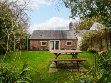 A garden with a wooden picnic table and a brick building with two small windows and a glass door at Goslings in Bradford Holsworthy
