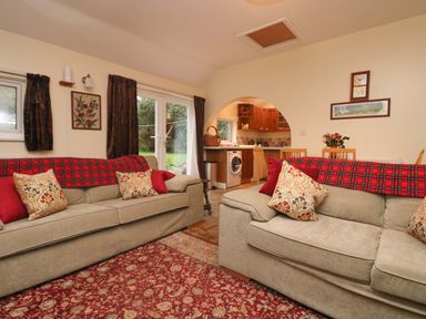 A living room with two sofas and a red patterned rug with an open kitchen visible through an arch at Goslings Bradford Holsworthy