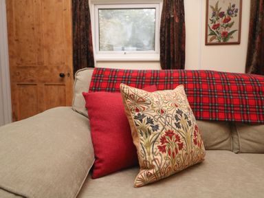 A beige sofa with two cushions and a red plaid blanket near a wooden door and a window at Goslings Bradford Holsworthy