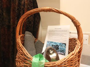 A wicker basket containing two grey mats a metal dog bowl a green bag and a printed paper with dog owner information at Goslings Bradford Holsworthy