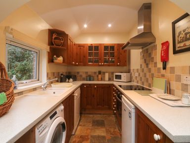 A kitchen with wooden cabinets a washing machine a dishwasher a microwave and a window at Goslings Bradford Holsworthy