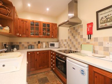 A kitchen with wooden cabinets a stovetop oven microwave fridge and a sink at Goslings in Bradford Holsworthy