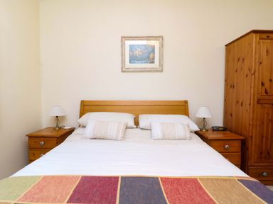 A bedroom with a wooden double bed white bedding two bedside tables with lamps an alarm clock and a wooden wardrobe at Goslings Bradford Holsworthy