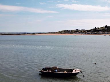 A small boat floating on a body of water with a sandy shoreline and houses in the background at Cool Stone Cottage in Instow near Bideford
