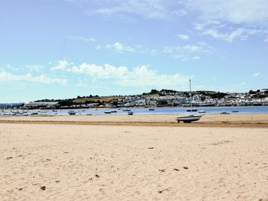 A sandy beach with boats on the shore and water with a town in the background at Cool Stone Cottage in Instow near Bideford