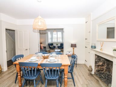 A dining room with a wooden table and blue chairs next to a fireplace at Cool Stone Cottage in Instow near Bideford