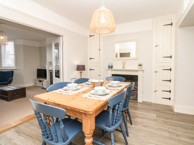 A dining room with a wooden table and blue chairs near a white fireplace at Cool Stone Cottage in Instow near Bideford
