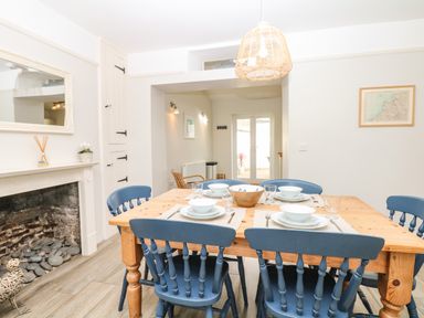 A dining room with a wooden table set for six with blue chairs and a fireplace at Cool Stone Cottage Instow near Bideford