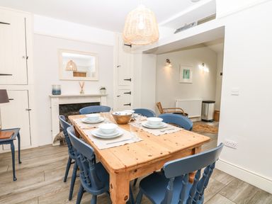 A dining area with a wooden table set for six and blue chairs at Cool Stone Cottage in Instow near Bideford