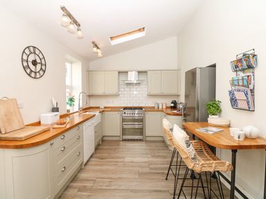 A kitchen with wooden countertops stools and a wall clock at Cool Stone Cottage Instow near Bideford