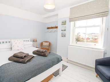 A bedroom with a bed with towels on it a wicker chair a window and a blue armchair at Cool Stone Cottage in Instow near Bideford