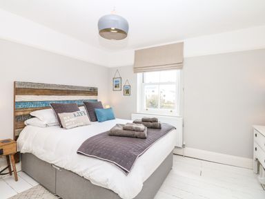 A bedroom with a bed with stacked pillows and folded towels near a window at Cool Stone Cottage Instow near Bideford