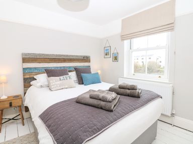 A bedroom with a bed with pillows a quilt and folded towels near a window at Cool Stone Cottage Instow near Bideford