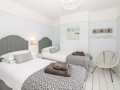 A bedroom with two single beds bedside table lamp wall art chair and hooks with hangers at Cool Stone Cottage Instow near Bideford