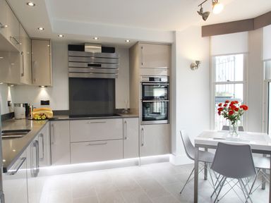 A kitchen with beige cabinets a stovetop oven and a dining table with chairs and flowers at 5 Arlington Villas in Ilfracombe