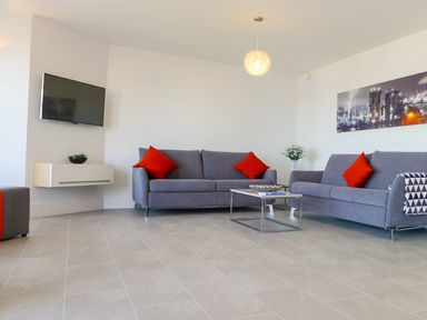 A living room with two gray sofas with red cushions a wall-mounted television and a coffee table at 5 Arlington Villas in Ilfracombe