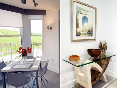 A dining area with a table and chairs next to windows with a view and a decorative glass table with art and bowls at 5 Arlington Villas Ilfracombe