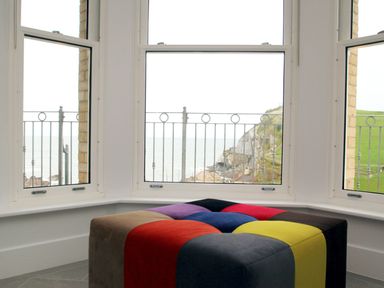 A corner window with a metal railing outside and a multicolored ottoman in front at 5 Arlington Villas in Ilfracombe