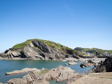 A coastal scene with rocky cliffs grassy hill and buildings in the background at 5 Arlington Villas in Ilfracombe