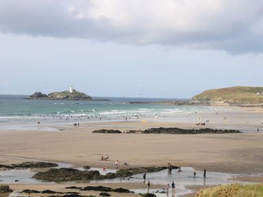 A beach with people on the sand and in the water with an island and lighthouse in the distance at Trevoole Barn in Praze An Beeble
