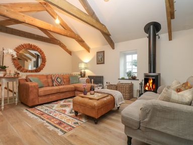 A living room with sofas a fireplace and wooden beams at Trevoole Barn in Praze An Beeble