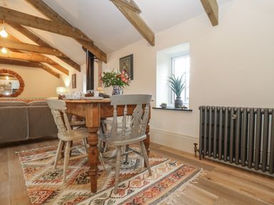 A dining area with wooden table and chairs on a patterned rug under wooden ceiling beams at Trevoole Barn in Praze An Beeble