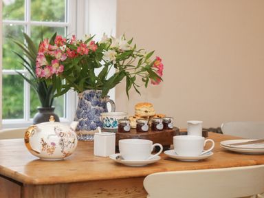 A wooden table with a teapot cups plates flowers and scones at Trevoole Barn in Praze An Beeble