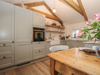 A kitchen with light gray cabinets a wooden table and exposed wooden ceiling beams at Trevoole Barn in Praze An Beeble