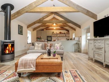 A living room with wooden beams a fireplace sofa and kitchen area at Trevoole Barn in Praze An Beeble