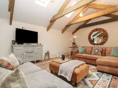 A living room with wooden beams a large mirror a leather sectional sofa a grey couch and a television on a wooden cabinet at Trevoole Barn in Praze An Beeble