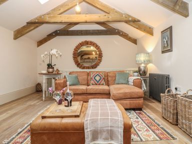 A living room with leather sofa and ottoman under wooden ceiling beams at Trevoole Barn in Praze An Beeble