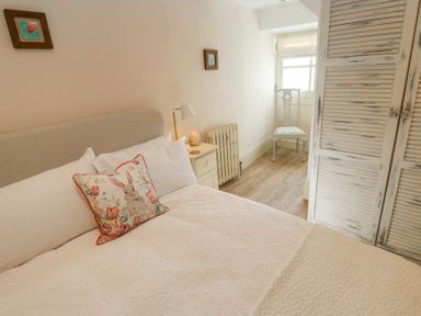 A bedroom with a bed with white bedding a floral pillow a bedside table with a lamp a wooden chair and a distressed wooden wardrobe at Trevoole Barn in Praze An Beeble