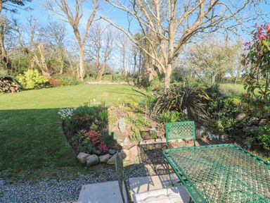 A garden with trees and flower beds and green metal table and chairs at Trevoole Barn in Praze An Beeble