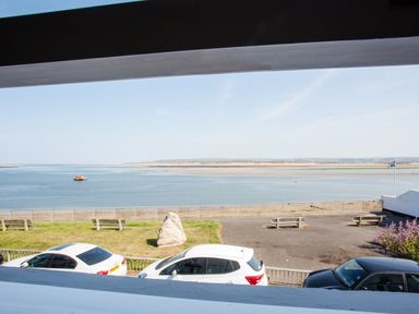A view of a waterfront with a river a boat benches parked cars and a flag at The Crab Shell in Appledore near Bideford