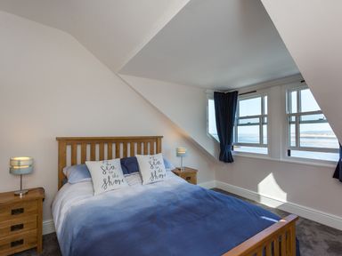 A bedroom with a wooden bed and blue bedding near windows overlooking the sea at The Crab Shell in Appledore near Bideford