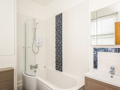 A bathroom with a bathtub shower combination a sink with a mirror and a window at The Crab Shell in Appledore near Bideford