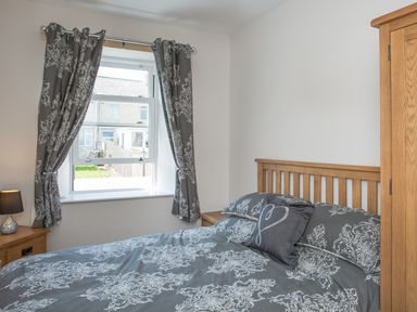 A bedroom with a bed a window with curtains a bedside table and a wooden wardrobe at The Crab Shell in Appledore near Bideford