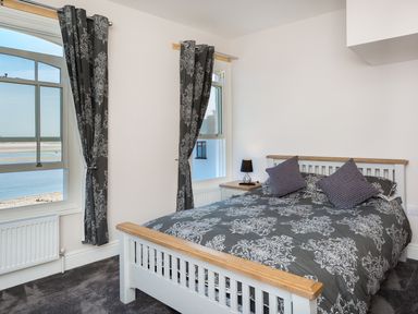A bedroom with a double bed beside two windows with patterned curtains at The Crab Shell in Appledore near Bideford