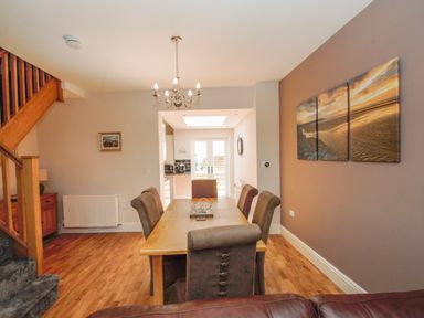 A dining room with a wooden table and six chairs a chandelier and a triptych beach painting on the wall at The Crab Shell in Appledore near Bideford