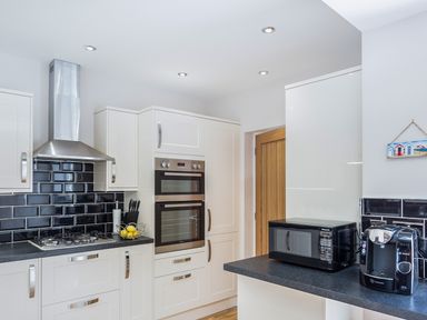 A kitchen with white cabinets black backsplash a microwave and coffee machine at The Crab Shell in Appledore near Bideford