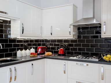 A kitchen with white cabinets black tiled backsplash a red toaster and kettle on the counter at The Crab Shell in Appledore near Bideford