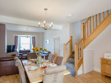 A dining table set with plates and sunflowers in a living room with leather sofas and wooden stairs at The Crab Shell in Appledore near Bideford