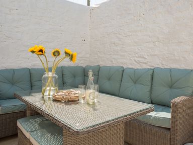 An outdoor seating area with a wicker table and corner sofa with cushions and sunflowers in a glass jar at The Crab Shell in Appledore near Bideford