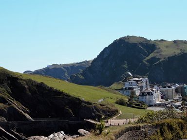 A coastal landscape with green hills buildings and rocky cliffs at Ocean Breeze in Ilfracombe