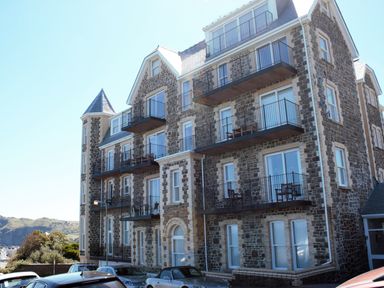 A stone building with multiple balconies and parked cars in front at Ocean Breeze in Ilfracombe