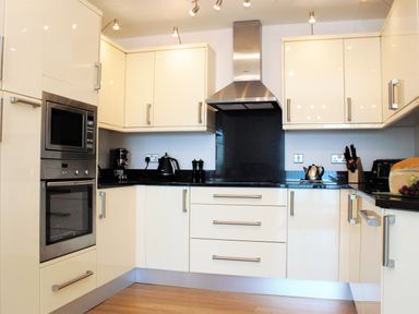 A kitchen with white cabinets a built-in oven and microwave a range hood and appliances on the black countertop at Ocean Breeze in Ilfracombe