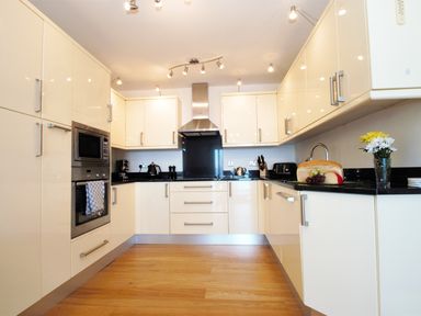 A kitchen with beige cabinets black countertops wooden floor and appliances at Ocean Breeze in Ilfracombe
