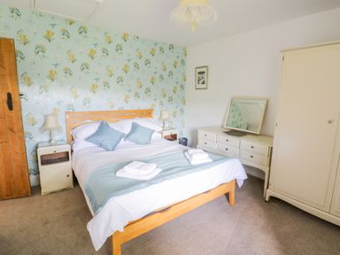 A bedroom with a wooden bed frame white and blue bedding a dresser with a mirror and wardrobe at Tai Ucha in Cerrigydrudion