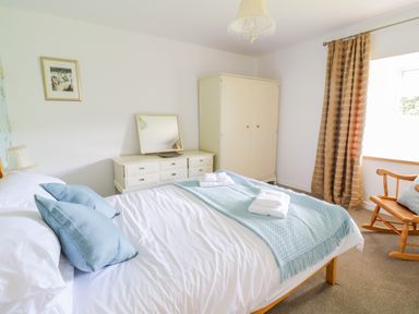 A bedroom with a bed with blue pillows and blanket a wardrobe a dresser with a mirror and a rocking chair at Tai Ucha in Cerrigydrudion