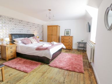 A bedroom with a double bed two wooden bedside tables wooden wardrobe wooden chest of drawers pink rugs and a wall-mounted tv at Tai Ucha in Cerrigydrudion